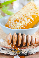Honeycomb in ceramic bowl and honey dipper on wooden background with cherry blossoms.