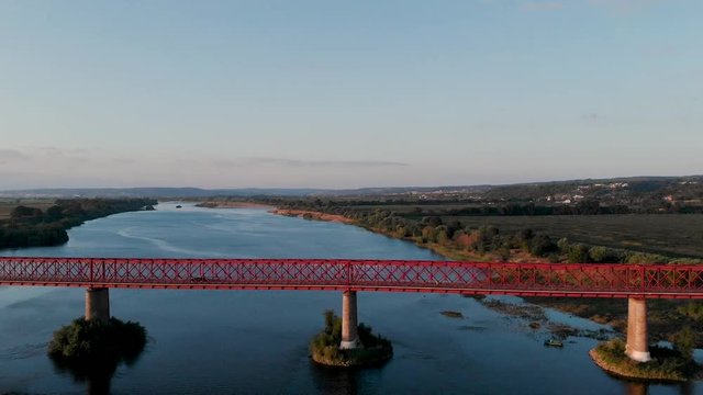 Zoom out of the red metal bridge, sunset time, in Goleg&atilde;, Santar&eacute;m, Portugal. Green landscape and river views. Soft and bright light. Chamusca bridge on tejo river