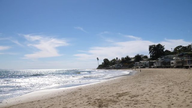Walking on the sand at Miramar beach with ocean waves crashing and expensive beach houses on the shore lining the coast of Montecito, California SLOW MOTION.