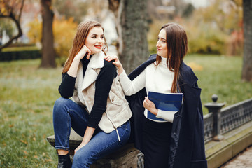 Beautiful girls in a park. Ladies near the fence. Women sitting