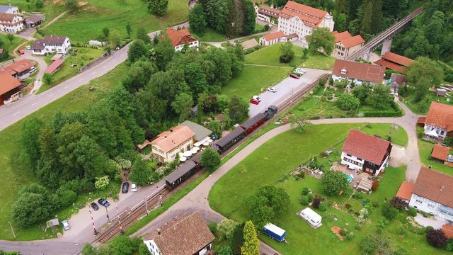 Drone shot from a very old Steam Locomotive with many wagons, near Bauma, at the station in Switzerland. Very nice location. Also visible an old spinning factory from the industialisation.