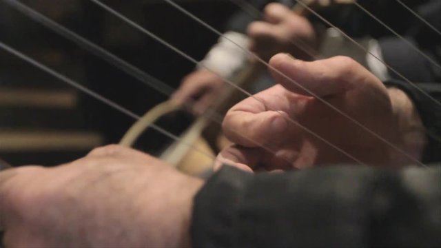 Close up of hands playing a traditional Georgian harp and the chuniri string instrument, with wrack focus on both instruments.
