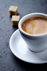 Cup of coffee and two brown sugar cubes on dark stone background. Close up. 