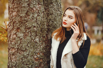 Beautiful girl in a park. Woman with phone. Girl at the tree