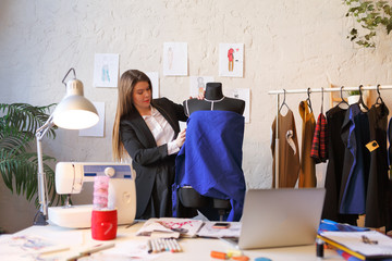 Image of long-haired seamstress woman standing next to mannequin with blue cloth .