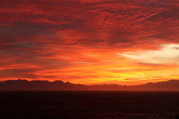 Fototapeta premium Beautiful bright orange sunrise over a bay with mountains in the background.