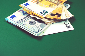 Euro notes and dollar bills on green background.