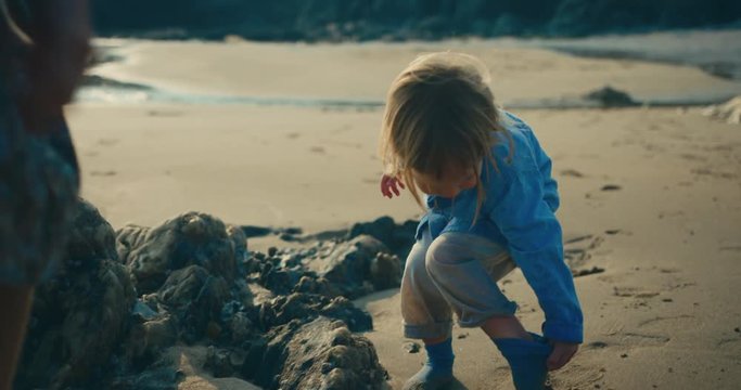Mother helping toddler take off his socks on the beach