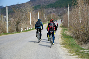 Group of young cyclists with backpacks and protective helmets are driving along an asphalt road in the village. Bike ride in early spring. Training in the fresh air. Selective focus.