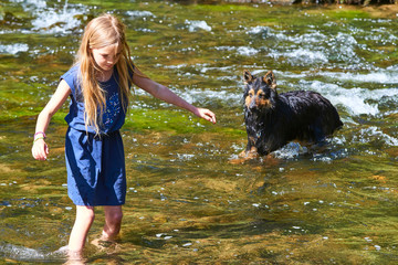 Child cute blond girl playing in the creek. Girl walking in forest stream, looking for pebbles and exploring nature. Summer children fun. Children summer activities