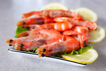 a plate of boiled shrimps with lemon close up, on a light gray table