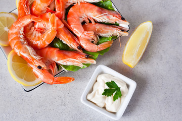 a plate of boiled shrimps with lemon and white sauce on a gray table, top view