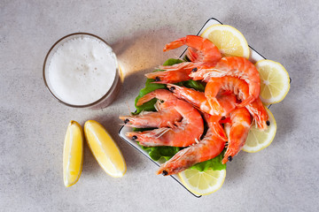 a glass of beer on the table with a plate of boiled shrimps with lemon top view