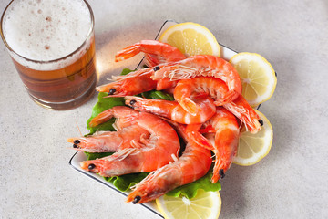 a glass of beer on the table with a plate of boiled shrimps with lemon on a light gray background