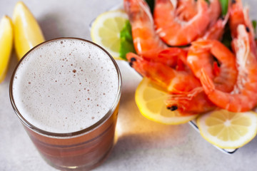 a glass of beer with foam on the background of boiled shrimps with lemon out of focus on the table, closeup