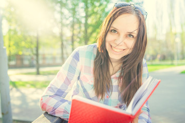 Obraz premium Woman with a book in his hands in the Park. Female, student is reading an interesting book sitting on the bench in the park