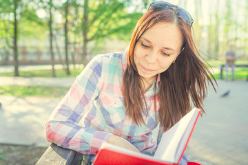 Woman with a book in his hands in the Park. Female, student is reading an interesting book sitting on the bench in the park