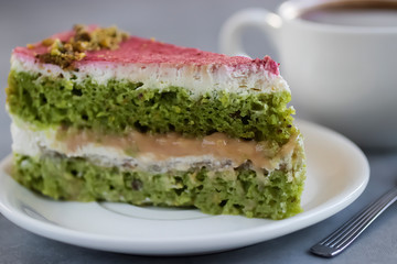 A piece of pistachio cake on a white plate and a cup of coffee.
