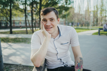 A young man sitting on a bench in the Park and looking at the camera. The concept of recreation in the Park