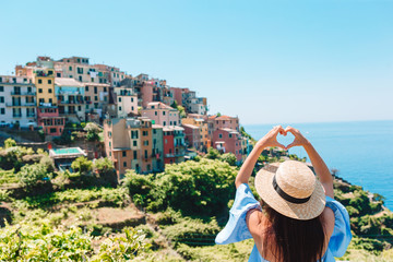Fototapeta premium Happy girl making with hands heart shape on the old coastal village in Cinque Terre National Park. European vacation.