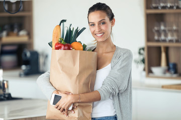 Beautiful young woman looking at camera while holding shopping bag with fresh vegetables in the...