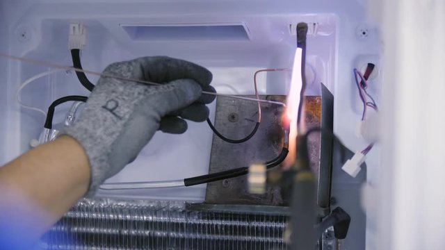 worker welds metal pipes for freon inside domestic fridge