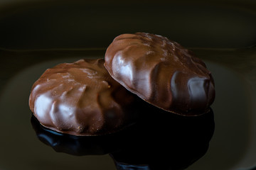 Marshmallow in chocolate icing on a black background with reflection.