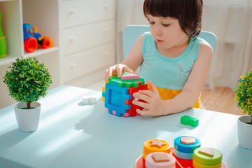 close-up of the child's hands collect puzzle sorter. Cube with inserted geometric shapes and colored plastic blocks.