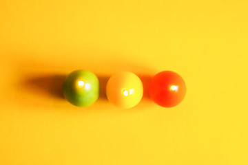 Traditional Easter decor. Group of bright burning paraffin candles in the shape of colorful eggs on yellow background.