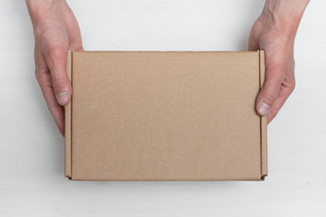 A parcel cardboard box in a delivery man hands on a white wooden table background. Delivery service concept.