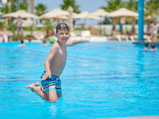 European boy jumping into swimming pool at resort. Moment of entrance in water.