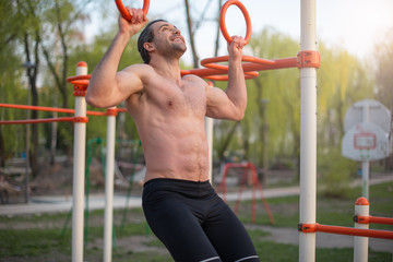 male athlete, torso with muscles, outdoor training, exercise on the rings