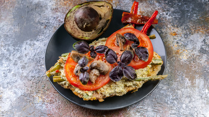 CloseUp tasty breakfast. Sandwich with tomatoes and mushrooms, basil and avocado on a dark plate.