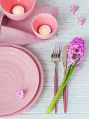 Pink rustic place setting with purple hyacinth flower, candles and linen napkin on white wooden background