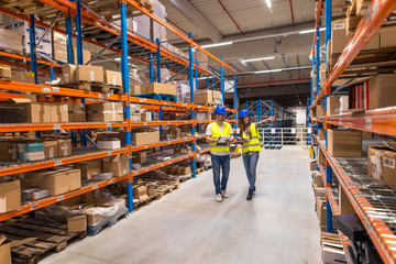 Working at warehouse. Two caucasian warehouse workers walking in distribution storage area discussing about logistics and organization.