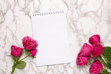 Pink roses and white notebook on a marble background