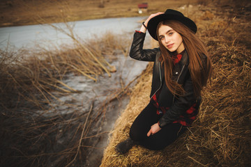 Lifestyle portrait of young woman in black hat resting by the lake on a nice and warm autumn day.