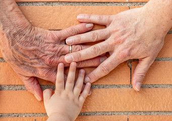 Three hands together, grandmother (elderly woman), mother, daughter, granddaughter. Family unity,...