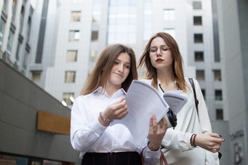 young students stand on the background of the college at the break, the girl peeps and writes off her homework