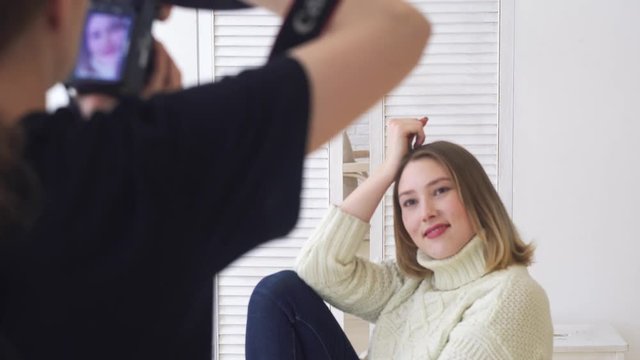 Close-up of female photographer taking picture of smiling model in white jumper and dark jeans in professional photo studio. Media. Professional photo session