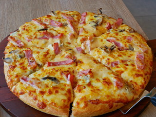 Close up of well-done fresh appetizing mushroom, ham, cheese pizza being served on a wooden tray, ready to eat