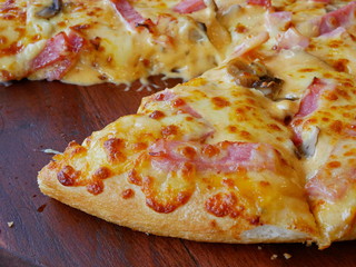 Close up of well-done fresh appetizing mushroom, ham, cheese pizza being served on a wooden tray, ready to eat