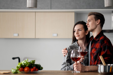 Beautiful young couple in plaid shirts in the kitchen preparing food and drinking red wine from glasses.