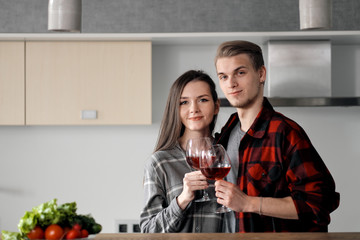 Beautiful young couple in plaid shirts in the kitchen preparing food and drinking red wine from glasses.