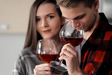 Beautiful young couple in plaid shirts in the kitchen preparing food and drinking red wine from glasses.