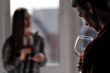 Young beautiful couple in plaid shirts on the balcony of a multistory building. Drink and taste wine, laugh and embrace.