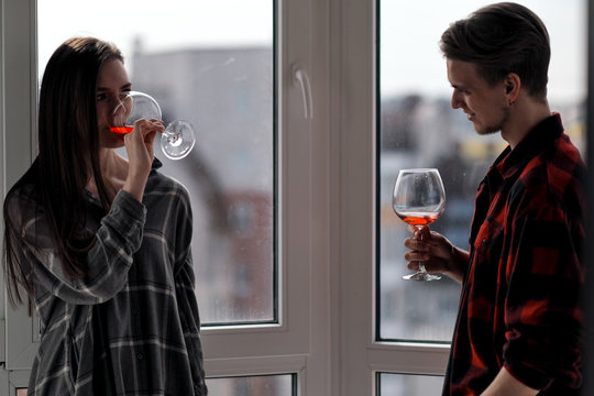 Young beautiful couple in plaid shirts on the balcony of a multistory building. Drink and taste wine, laugh and embrace.