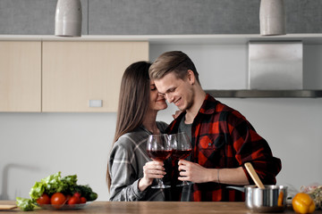 Beautiful young couple in plaid shirts in the kitchen preparing food and drinking red wine from glasses.