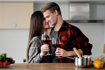 Beautiful young couple in plaid shirts in the kitchen preparing food and drinking red wine from glasses.