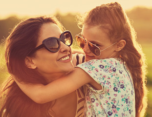 Happy fashion kid girl embracing her mother with strong love in trendy sunglasses smiling and...